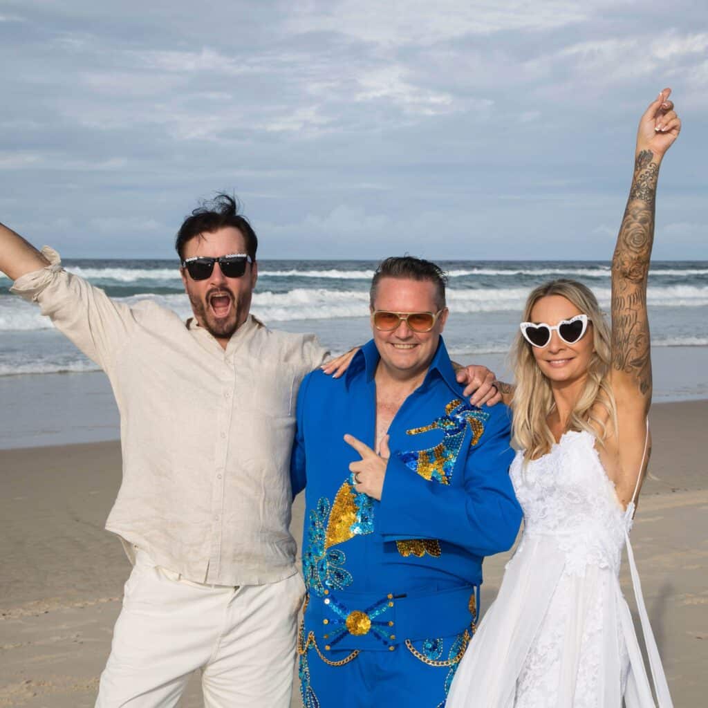 Mark Reynolds MR Celebrant dressed as Elvis at a beach wedding with the bride and groom cheering.