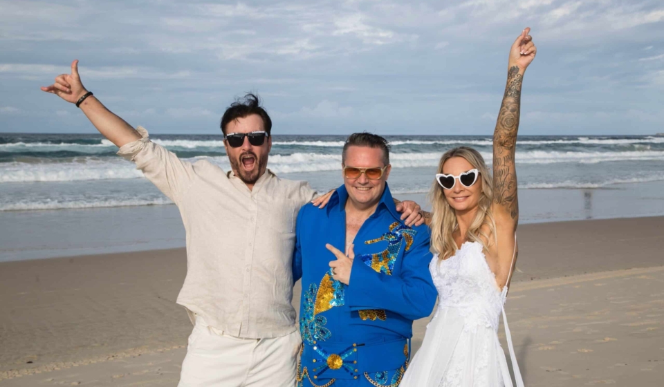 Mark Reynolds MR Celebrant dressed as Elvis at a beach wedding with the bride and groom cheering.