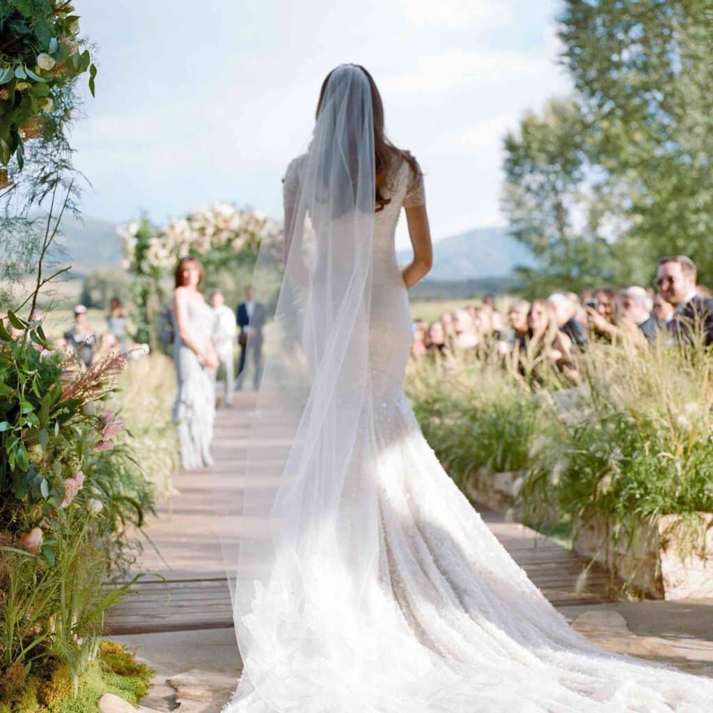 A bride walking down the aisle on her wedding day in a white wedding dress with guests in the background