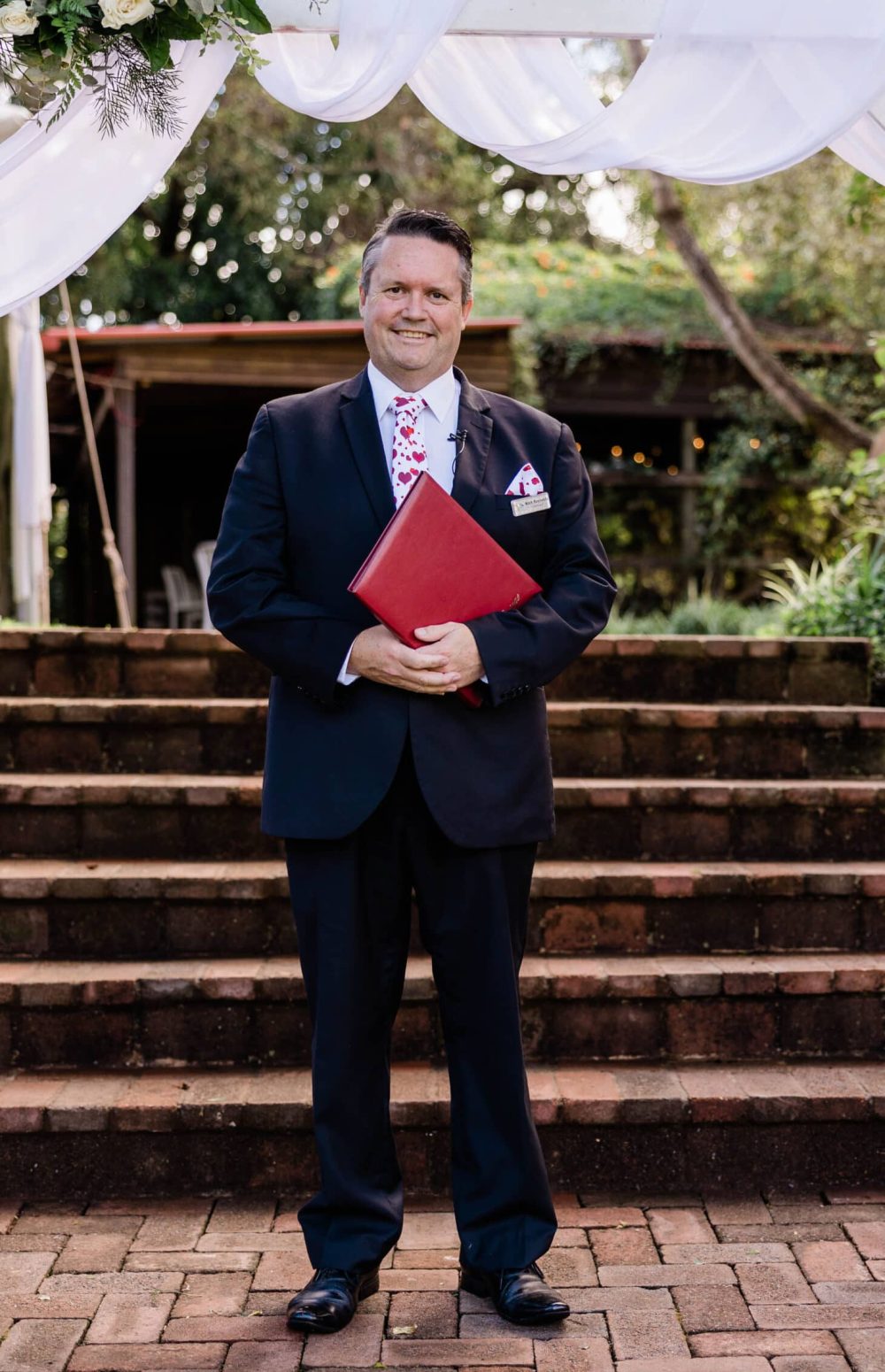 Mark Reynolds Celebrant in a black suit standing on the steps of one of the ceremony areas at the Secret Garden Wedding Venue on Mt Tamborine.